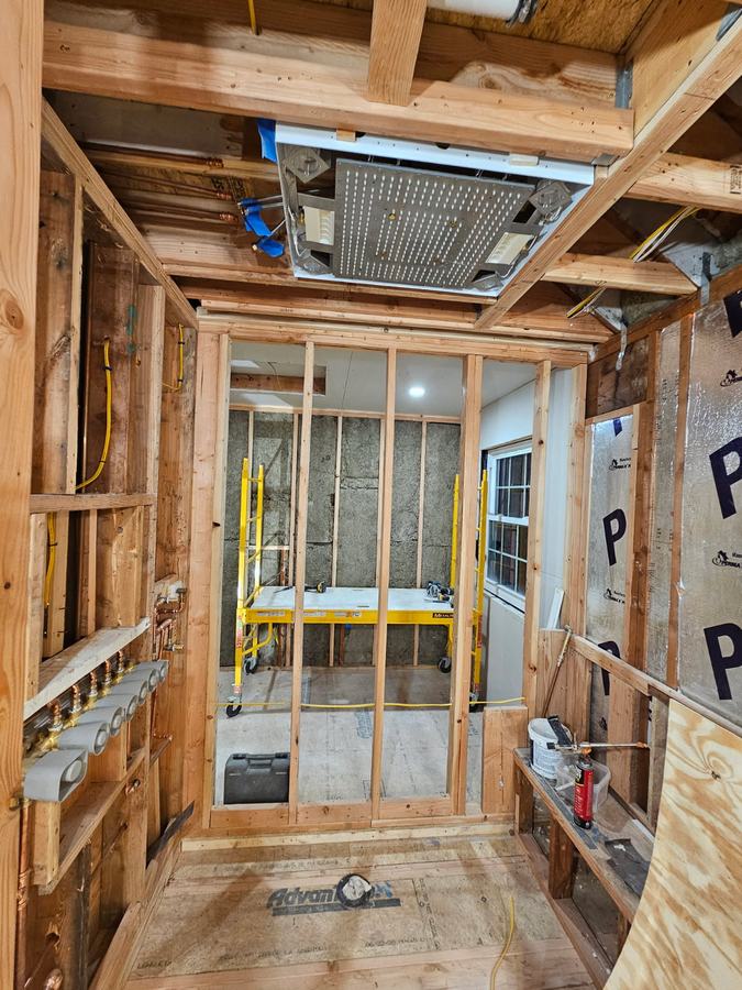 Interior framing and mechanical rough-in on a Long Island renovation — open studs, copper manifold, wiring and ductwork exposed before inspection